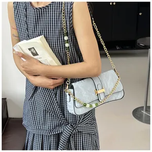 Détail du sac baguette bleu clair avec texture plissée et chaîne à perles sur robe à carreaux