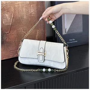 Détail du sac baguette blanc avec chaîne dorée, perles vertes et accents sur cuir