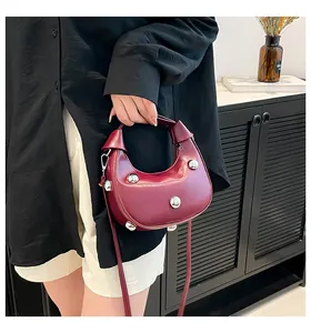 Détail macro du sac demi-lune en cuir bordeaux avec clous argentés et poignée nouée