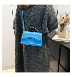 Model wearing bright blue crossbody bag with unique wavy flap and leather strap
