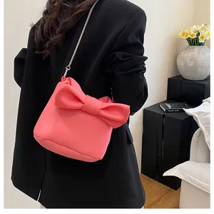 Detail of coral pink bow bag featuring a fine metal chain strap and matte texture