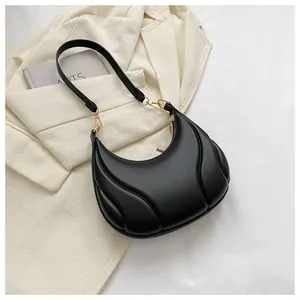 Détail du sac hobo noir avec texture matelassée et accents dorés sur un blazer blanc