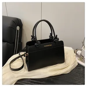 Detail of black faux leather handbag showing knotted handle and gold fashion lettering