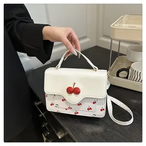 Detail of white PU crossbody bag featuring red cherry prints and 3D cherry charm accessory