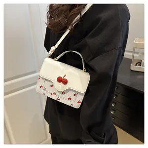 Close-up of white crossbody bag featuring cherry print and a 3D cherry ornament detail