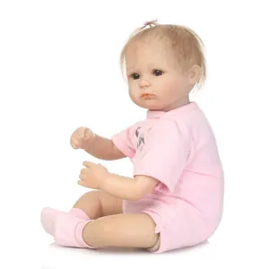 Poupée bébé reborn réaliste en body rose assise sur un fond blanc neutre