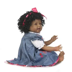 Muñeca realista de piel oscura con pelo rizado, vestido vaquero y lazo rosa