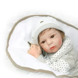 Realistic reborn baby doll with brown hair in green striped outfit on white plush background
