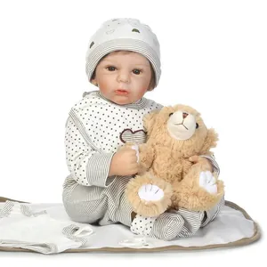 Lifelike reborn baby doll in striped outfit with plush bear and pacifier on white mat