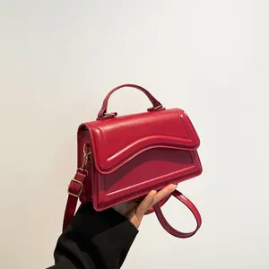 Modern red leather square handbag with wavy edge and gold hardware, handheld front view
