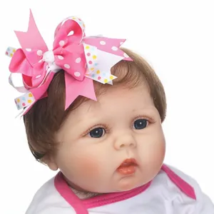 Realistic baby doll wearing a multilayered pink polka dot bow headband accessory