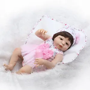 Lifelike reborn baby doll in pink floral dress with bottle on white faux fur background