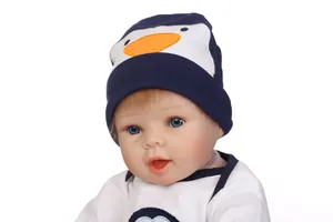 Close-up of realistic reborn baby doll wearing a blue penguin knit hat and white top