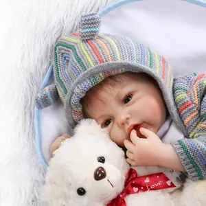 Realistic reborn baby doll in striped knit hoodie with a small plush teddy bear
