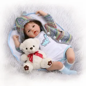 Realistic reborn baby doll in grey stripe cardigan with plush bear on a soft rug