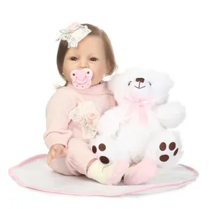 Realistic reborn baby doll in pink knit outfit with white teddy bear on soft white mat