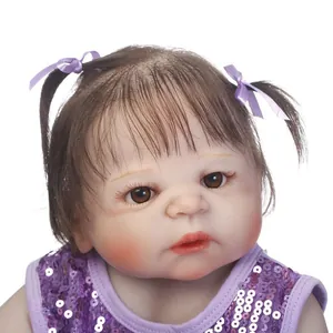 Realistic reborn baby doll with brown eyes and purple sequin vest on white background