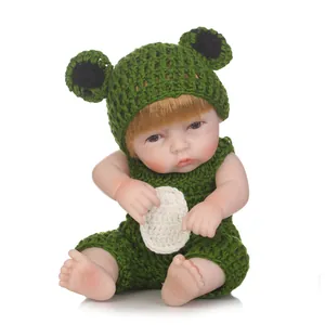 Realistic reborn baby doll wearing a green knitted frog outfit on a white background