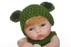 Close-up of lifelike baby doll wearing green crochet frog hat and knit outfit