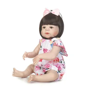 Muñeca bebé reborn realista con pelo corto negro, lazo rosa y pelele floral en fondo blanco