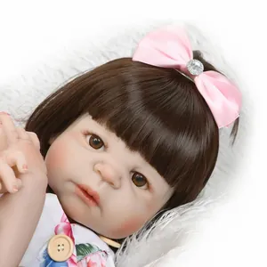 Muñeca bebé Reborn realista con pelo castaño, diadema rosa y ropa floral sobre alfombra blanca