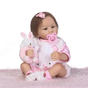 Realistische reborn babypop in roze stippenoutfit met pluche konijn op zacht tapijt