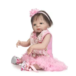 Realistic reborn baby doll with brown hair and pink floral dress on white background