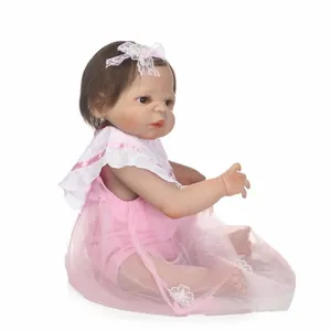 Realistic reborn baby doll with brown hair in a pink lace dress on white background