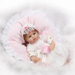 Realistic reborn baby doll in lace dress with pink hat and feeding bottle on white plush mat