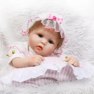Realistic reborn baby doll in lace white outfit lying on a soft pink striped pillow