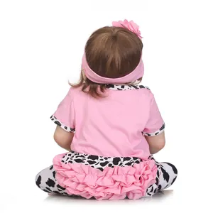 Back view of lifelike reborn baby doll in cow print pants and pink floral headband