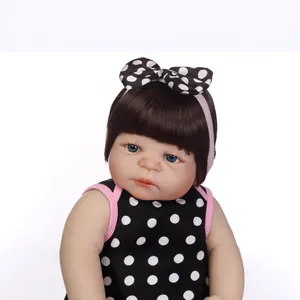 Realistic reborn baby doll with dark brown hair and polka dot dress on white background