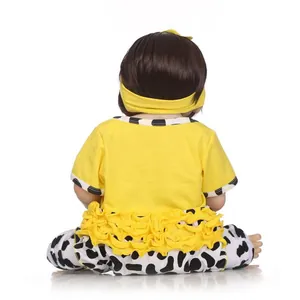 Poupée réaliste vue de dos portant un t-shirt jaune et un pantalon à motif vache et bandeau