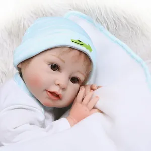 Realistic reborn baby doll in striped blue hat with crocodile embroidery on soft plush rug