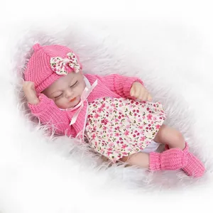 Mini bambola reborn realistica con cappello rosa e vestito floreale su morbido tappeto