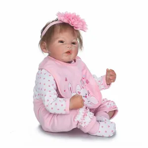 Realistic reborn baby doll in pink romper with flower headband on white background