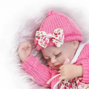 Bambola realistica che dorme con cappello e cardigan rosa su sfondo di peluche bianco