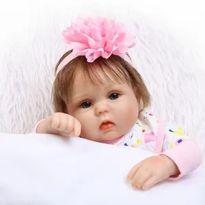 Lifelike reborn baby doll in floral outfit with pink flower headband on soft white plush