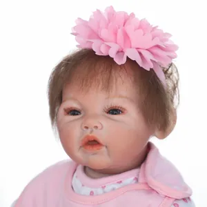 Realistic reborn baby doll with brown hair and pink floral headband in close-up shot