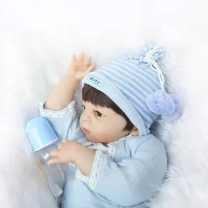 Realistic reborn baby doll in blue knit sweater and hat lying on white plush background