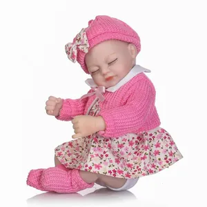 Bambola realistica con vestito rosa in maglia e cappello a fiori su sfondo bianco