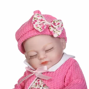 Bambola realistica che dorme con cappello in maglia rosa e vestito floreale coordinato