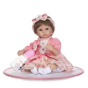 Lifelike reborn baby doll in pink floral dress and cardigan sitting on a soft cushion