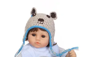 Detail einer handgemachten Baby-Häkelmütze mit Ohrenklappen und Tiermotiv auf Puppe