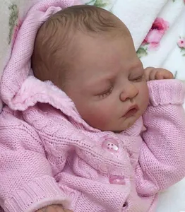 Lifelike sleeping reborn doll kit in a pink cable knit hooded sweater on floral blanket