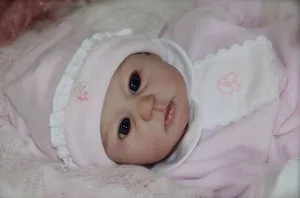 Poupée reborn réaliste aux yeux bleus portant un bonnet rose à pois et un body fleuri