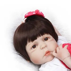 Lifelike reborn baby doll with brown hair and red polka dot bow on white plush background