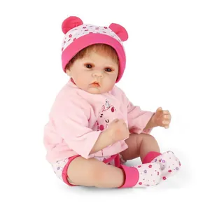 Realistic reborn baby doll in pink plush outfit with floral hat on white background