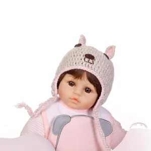 Lifelike baby doll with grey knitted animal hat and pink striped outfit on white backdrop