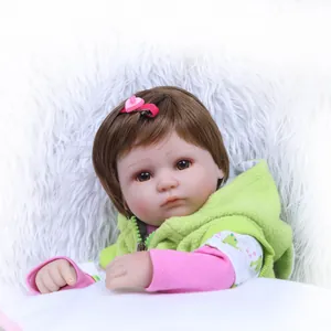 Lifelike reborn baby doll in green hoodie with heart hairclip on white plush background